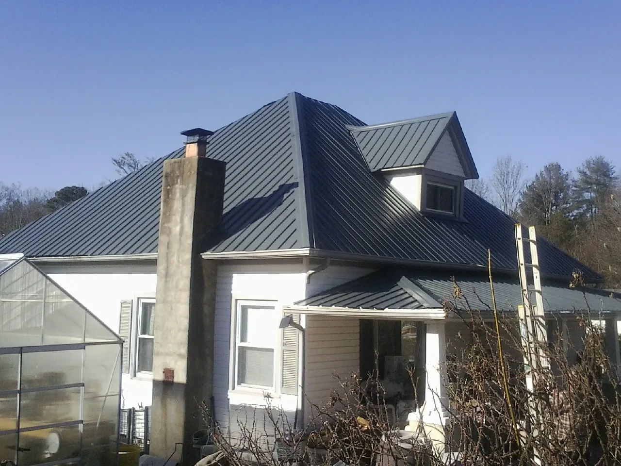 Dark blue standing seam metal roof on a white farmhouse with dormer — Slate & Tile Roof Repair by Roofing Brothers in Continental