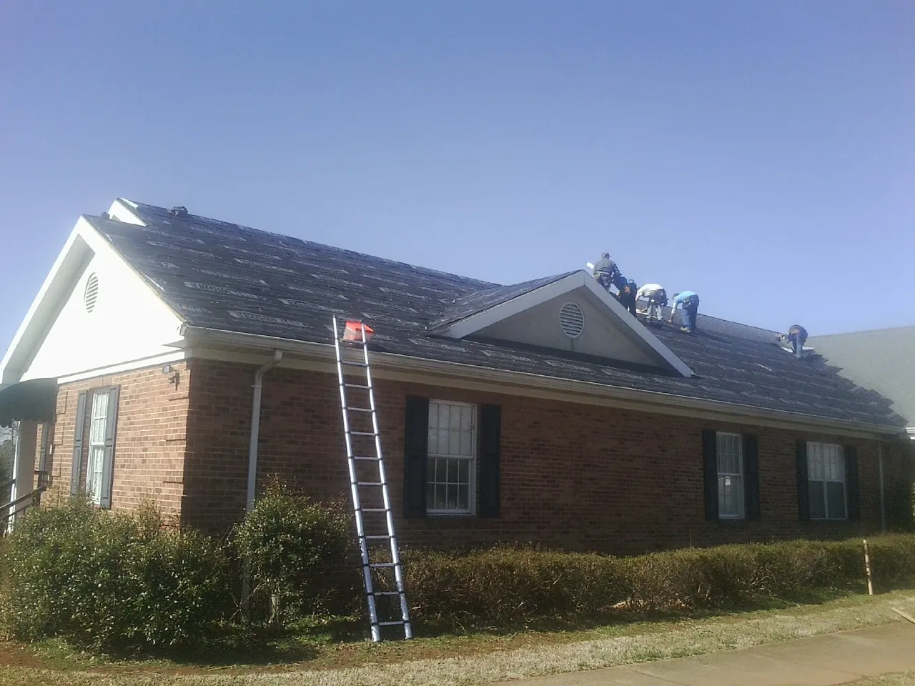 Crew tearing shingles off a brick ranch roof with a ladder set — Metal Roof Repair work by our crew in Continental