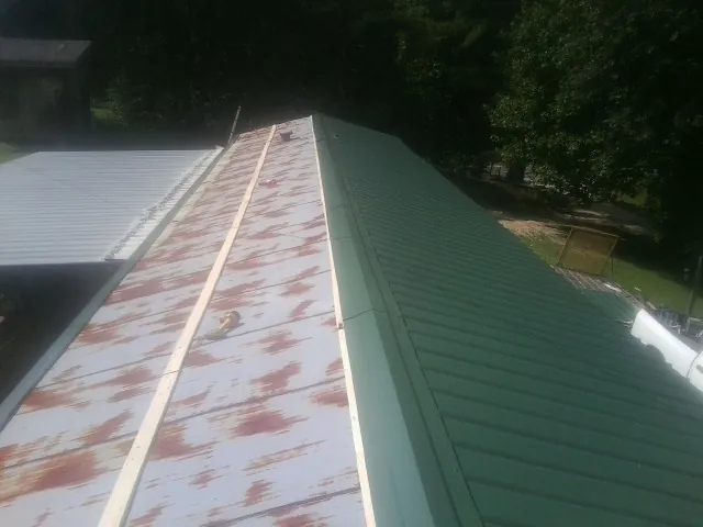 Old rusted panels beside newly installed green metal roofing — Wind Damage Roof Repair by Roofing Brothers in Continental