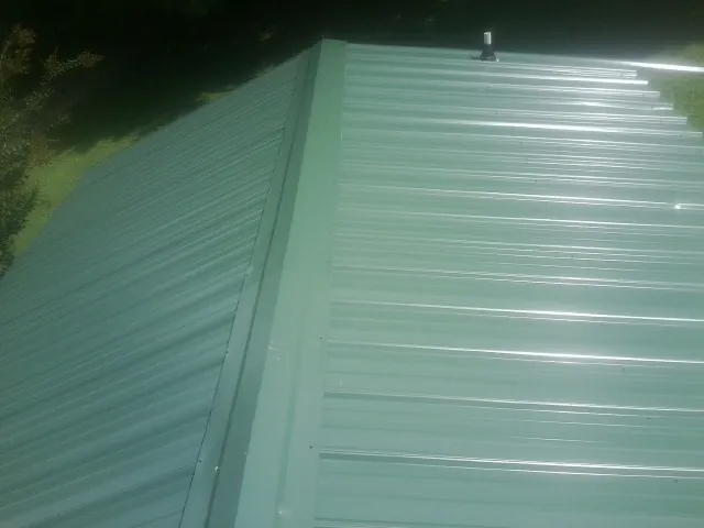 New green metal panels meeting at the ridge of a roof — Flat Roof Repair work by our crew in Continental