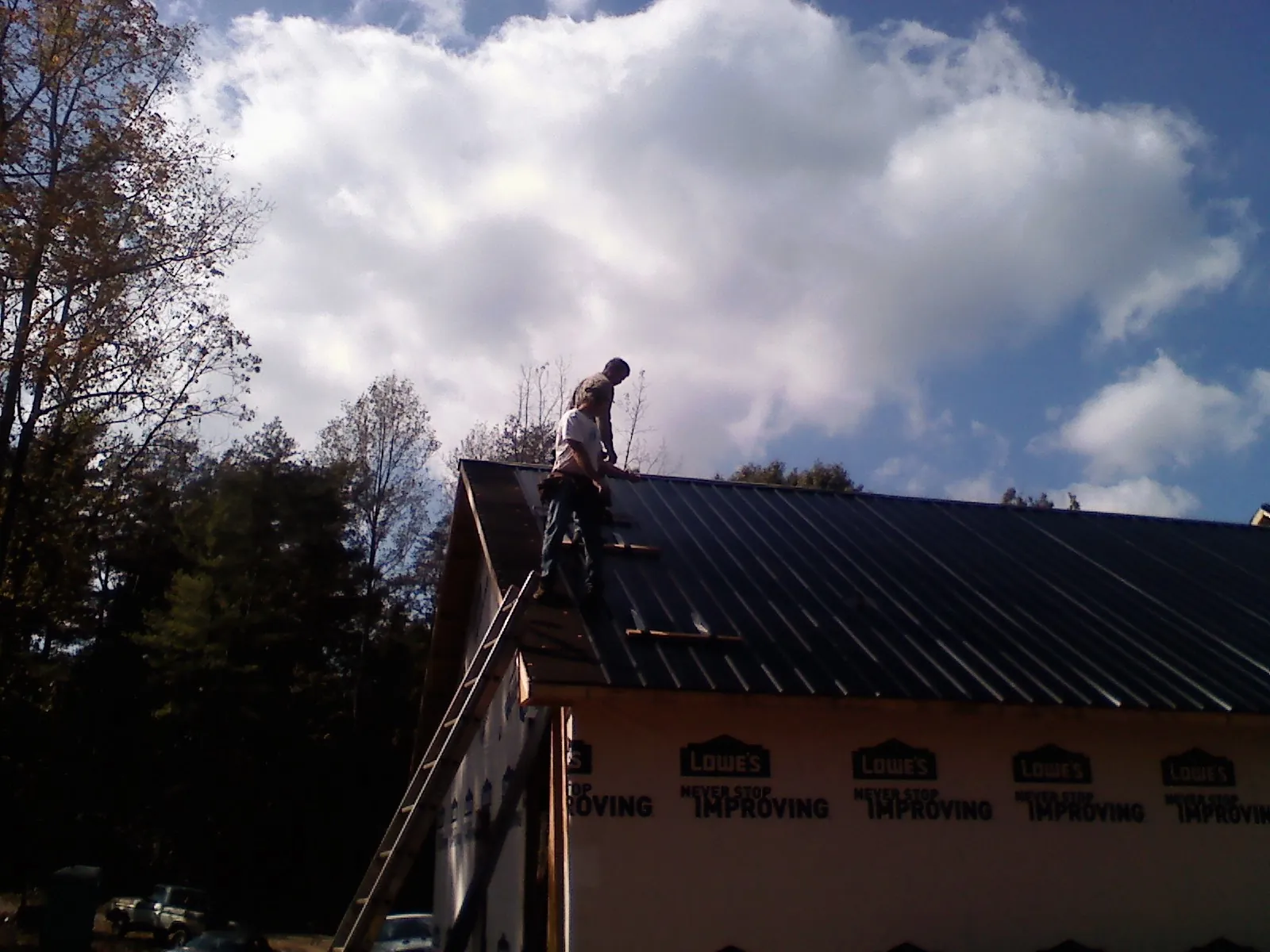 Roofer fastening dark metal panels high against a cloudy sky, from a Roof Inspection job in Continental