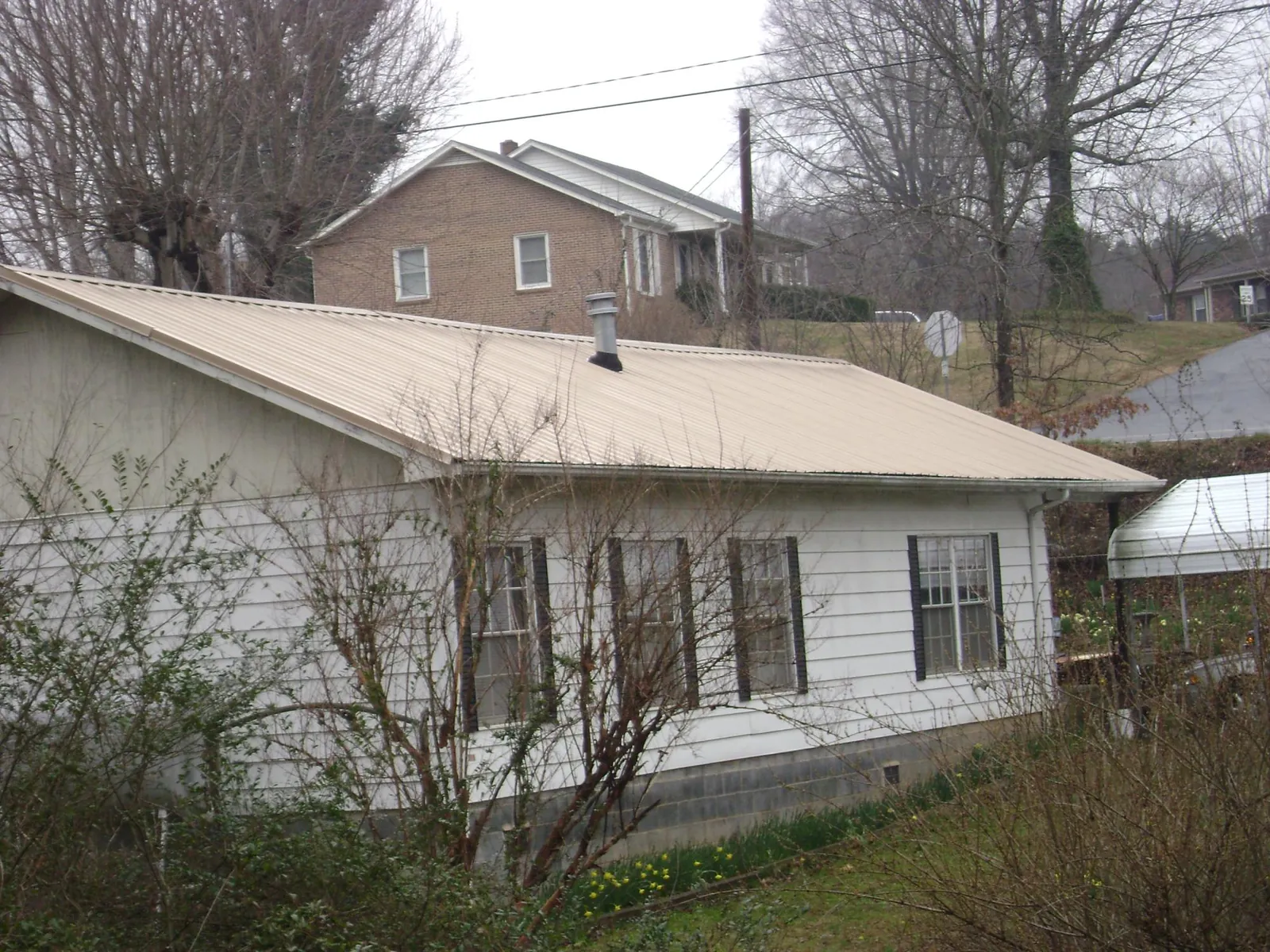 Tan metal roof on a white sided house set into a hillside — Commercial Roofing by Roofing Brothers in Continental